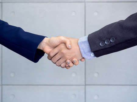 Businessman and businesswoman are shaking hands in office wall background. Handshake between...