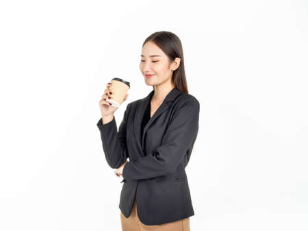 Young Asian smiling businesswoman in suit drinking coffee isolated on white background. Portrait of attractive business lady holding disposable paper coffee cup.の写真素材