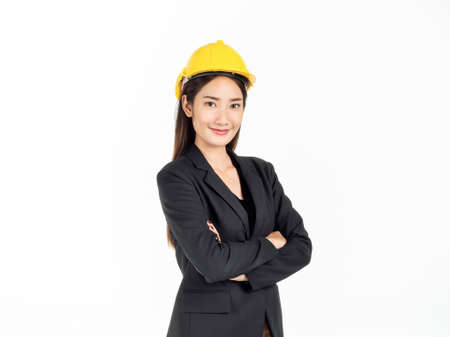 Young Asian businesswoman smiling wearing black suit and yellow safety helmet standing with her arms folded. Portrait of female engineer looking confident isolated on white background.の写真素材