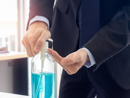 Hand disinfection with alcohol gel. Businessman's hands using the sanitizer on table in office, coronavirus prevention. A business man using gel hand washing to protect against the Covid-19 virus.の写真素材