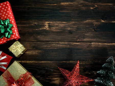 Christmas and happy new year background. Top view of beautiful red and gold gift boxes with shiny green,red and gold bow and star and small fir tree on dark wooden plank background with copy space.の写真素材
