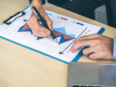 Business man and womanâ€™s hands using pen pointing for checking report chart and notebook...