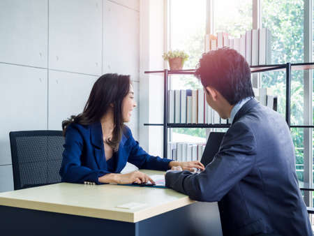 Asian business woman and businessman working together in office. Young male employee and female boss wearing suit looking laptop computer on desk.の写真素材