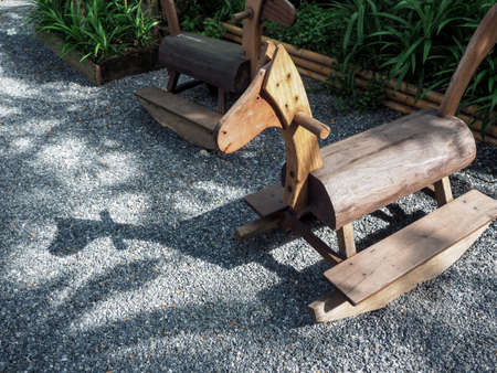 Empty lonely old classic homemade wooden rocking horse on gravel ground near the green garden with copy space.の写真素材