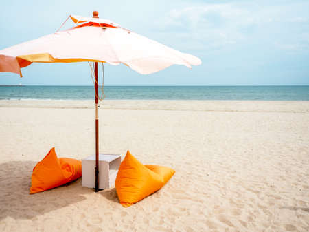 Orange beach umbrellas and bean bag chairs on the sand beach on blue sky background with copy space, minimal style.の写真素材