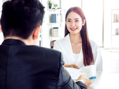 Young attractive Asian woman handing resume to businessman in suit during job interview in office. Beautiful female candidate smiling while interviewing job. Business, career and placement concept.の写真素材