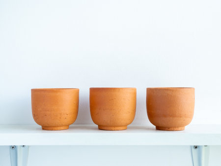 Three empty small modern terracotta pots on white wood shelf isolated on white wall background with copy space.の写真素材
