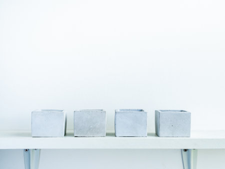 Four of empty modern geometric concrete planters on white wood shelf isolated on white wall...