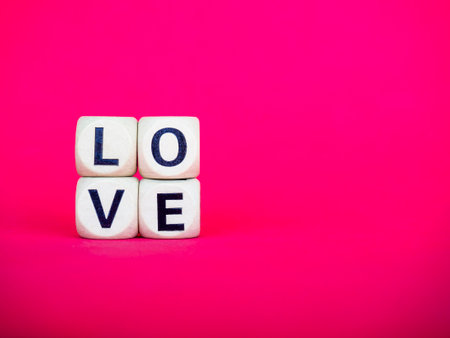 Love word written on wood block on pink red background with copy space, minimal style. Love, text is written in black letters on wooden cubes.の写真素材