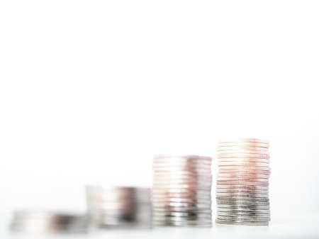 Coin stacks isolated on a white background with copy space, focus on highest stack. Piles of silver money arrange as a graph growth with success light.の写真素材