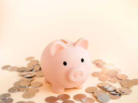 Cute piggy bank, pink color with piles of thai baht coins on soft beige background with copy space. Saving money, Investment and finance concept.の写真素材