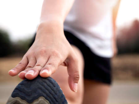 Close up hand stretching leg and feet before a workout. Closeup finger touching on running shoes of...