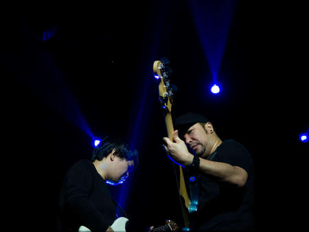 Two Asian musician man, bass and guitarist playing solo bass guitar on stage with blue light on dark background. Music performance in rock band concert.の写真素材
