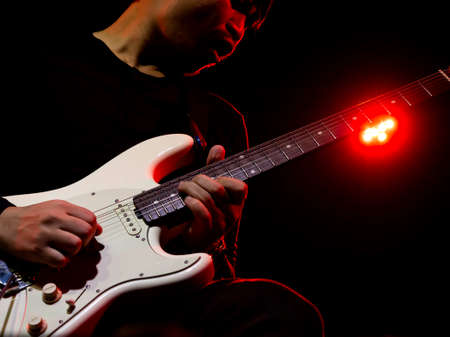 Asian musician man, guitarist playing solo guitar on stage with red light on dark background with copy space. Music performance in rock band concert.の写真素材