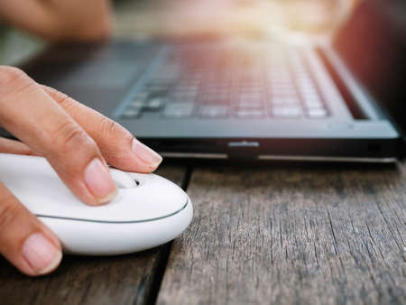 Close up finger using modern white wireless mouse while working on black laptop computer on wooden...