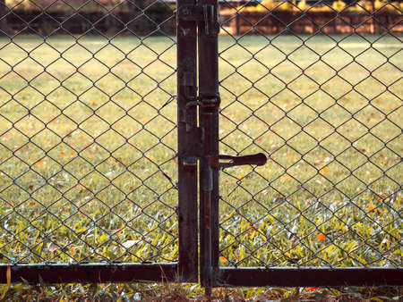 Closed old outdoor fence gate. Rusty chain link fence on grass background.の写真素材