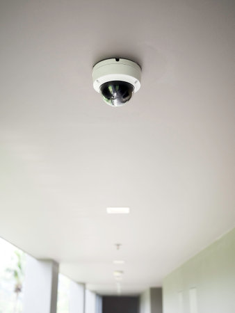 CCTV camera on white ceiling at walkway on ground floors in apartment building with copy space, vertical style.の写真素材