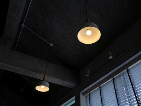 Modern round ceiling light with light bulb hanging from concrete construction in the dark room near...