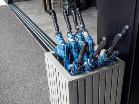 Many blue folded umbrellas in umbrella stand container box stored service prepare for guest to...