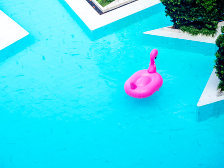 Empty lonely pink inflatable flamingo floating in modern pool, top view with copy space. Summer pool...