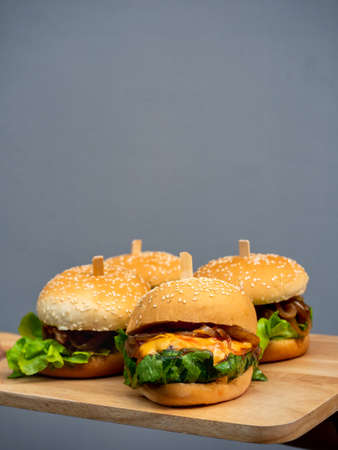 Delicious fresh homemade burger set. Hand holding and showing tasty four homemade hamburgers on wooden tray or wood cutting board on grey background with copy space, vertical style.の写真素材
