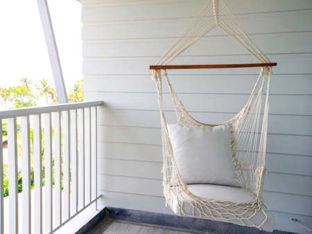 Empty white knitting rope swing hanging from ceiling on white wood background in room terrace in the resort. Vintage white handcraft hammock decoration on balcony.の写真素材