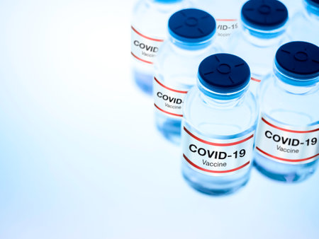 Covid-19 vaccine. Modern label Covid-19 vaccine on bottle vials on illuminate light table in a research medical lab with copy space, blue tone. Development and creation of a coronavirus vaccination.の写真素材