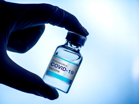 Covid-19 vaccine. Modern blue label Covid-19 vaccine on bottle vial showing by scientist or doctor hand wearing gloves in the lab, dark blue tone. Development and creation of coronavirus vaccination.の写真素材