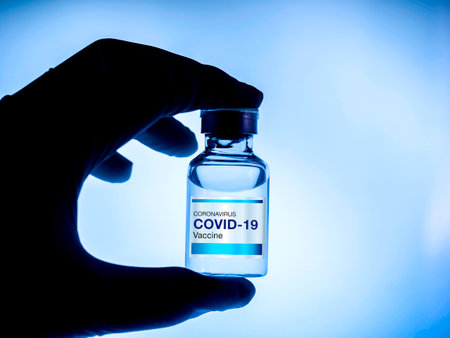 Covid-19 vaccine. Modern blue label Covid-19 vaccine on bottle vial showing by scientist or doctor hand wearing gloves in the lab, dark blue tone. Development and creation of coronavirus vaccination.の写真素材