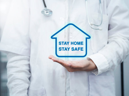 Message STAY HOME STAY SAFE in a home symbol on the doctor's hand in a white coat and medical stethoscope. Stay safe, self-protection, self quarantine and social disdancing concept.の写真素材