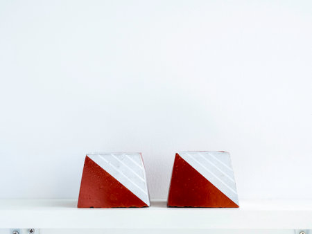 Empty DIY concrete pots, pyramid shape on a white wooden shelf on white wall background with copy...