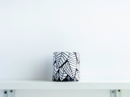 Empty DIY round shape concrete pot with leaves drawing isolated on a white wooden shelf on white wall background with copy space. Unique color painted cement planter.の写真素材