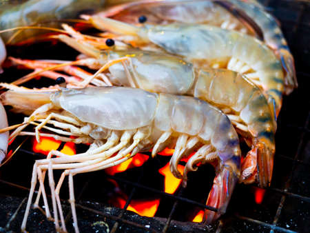 Grilled prawn on flaming grill. Close-up row of raw river prawns are being grilled on the grille on...