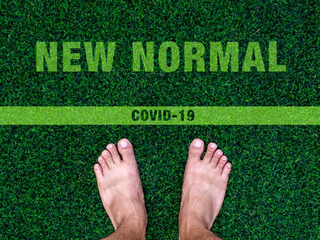 Crossing to the new normal concept. Bare feet on artificial green grass with text "New Normal" and line, after COVID-19 coronavirus pandemic situation concept.の写真素材