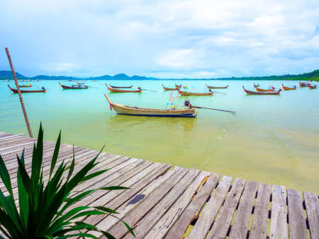 Beautiful seascape summer background. Close up empty wooden plank bridge with local fisherman boat on the sea and sky background on a sunny day in Thailand.の写真素材