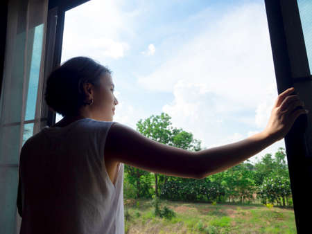 Image of back of Asian woman short hair opening a large glass window in the bedroom on second floor...