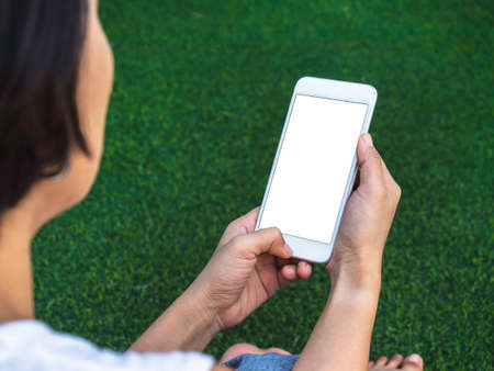 Mockup image of phone. Close-up white blank screen on mobile phone in hands on green artificial...