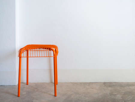 Empty DIY chair orange color made from steel and wire on concrete floor and white wall background...