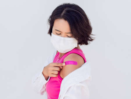 Vaccinations concept. Vaccinated Asian woman wearing a face mask, pink sleeveless and white shirt...