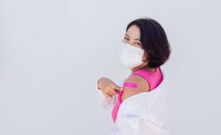 Vaccinations concept. Vaccinated Asian woman wearing medical face mask, pink sleeveless pointing at...