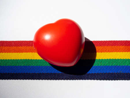 Clpose-up red ball heart on rainbow stripe ribbon isolated on white background. LGBT concept with...