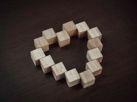 Wooden blocks arranged in heart shape on dark wood background, top view. Love and coexistence concept.の写真素材