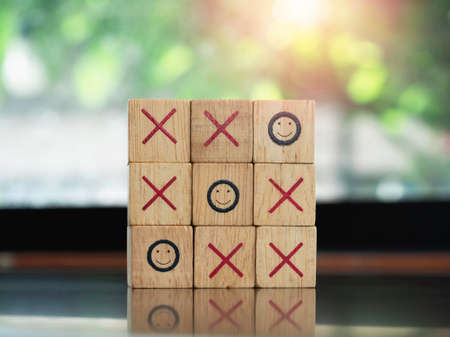Three smiling face icons on tic tac toe wooden block game on wood table on green nature background. Winner, strategy and business goal concept.の写真素材