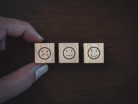 Services rating, ranking, review, feedback and customer satisfaction survey concept. close up finger choosing not satisfied face emoticon icon on wooden cube block on dark wood background, top view.の写真素材