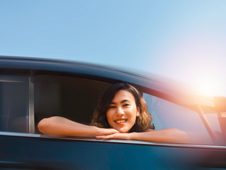 Journey of happy Asian woman with short hair with blur motion from black car movement on blue sky background. Female travelers enjoy and smiling while looking at the camera, on sunny days.の写真素材