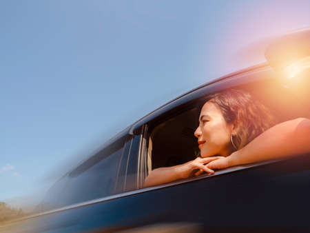 Journey of happy Asian woman with short hair with blur motion from black car movement on blue sky background. Female travelers enjoy and smiling while looking at the view outside, on sunny days.の写真素材