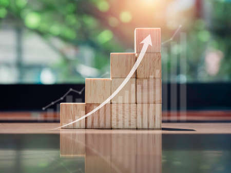 Growth chart and graph. Glowing rise up arrow on the top of wooden blocks chart steps on wooden desk with copy space, eco style. The business growth process, finance, and economic improvement concept.の写真素材