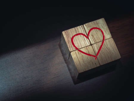 Red heart on wooden cube blocks on dark brown wood background.の写真素材