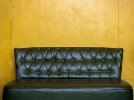 Dark green vintage leather sofa seat with pins and buttons on yellow wall background in the living room with copy space.の写真素材