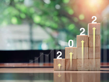 Growth chart and graph. Glowing rise up arrow on the top of wooden blocks chart steps on wooden desk, the year 2022, eco style. The business growth process, finance, and economic improvement concept.の写真素材